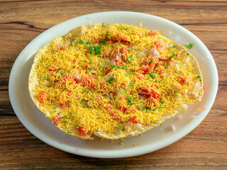 Masala Papad is a delicious Indian snack made using roasted or fried papad topped with a tangy and spicy onion tomato mix, served over a rustic wooden background, selective focus