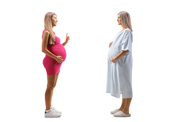 Full length profile shot of a pregnant woman in a patient gown and a pregnant woman in a pink dress talking