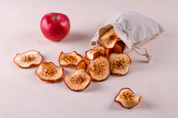 Slices of dried fruit apples in an eco-friendly bag and one ripe red apple lie on a light surface. Useful products, environmental protection, recycling concept. Selective focus.