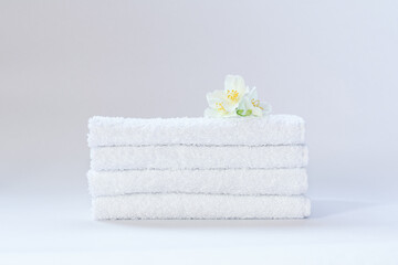 Four white neatly folded terry towels with a jasmine flower on a light background.