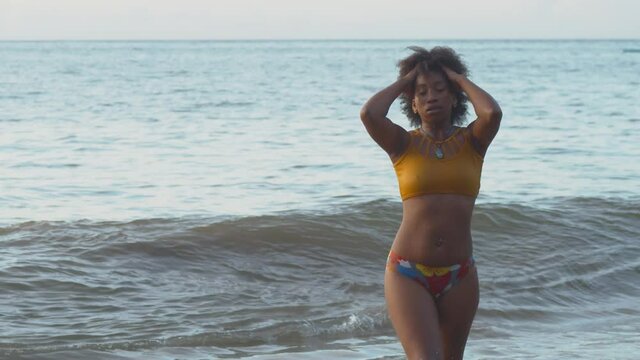 Muscular female in a bikini walks out of the ocean while passing her hand in her hair