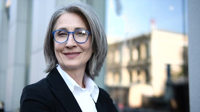 Closeup face of mature gray haired woman teacher in eyeglasses looking at camera