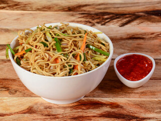 Veg Hakka Noodles a popular oriental dish made with noodles and vegetables, served over a rustic wooden background, selective focus