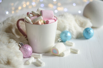 Cup with marshmallows, pinky and blue balls on a white table.