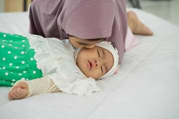 Muslim new born baby girl wearing HIJAB with sister kissing sleeping on white bed at home. 