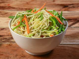 Veg Noodles a popular indo-chinese dish made with noodles and vegetables, served over a rustic wooden background, selective focus