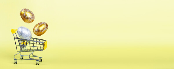 Easter golden and silver eggs levitation to the shopping cart on yellow background. Easter concept. Copy space. banner