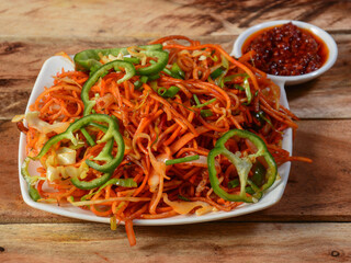 Schezwan Veg Noodles a popular indo-chinese dish made with noodles, vegetables and schezwan sauce, served over a rustic wooden background, selective focus