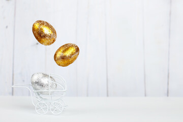 Easter golden and silver eggs levitation in the white baby stroller on a light wooden background. Newborn concept