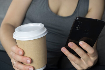young woman sits on the sofa with a glass of coffee and looks at her smartphone
