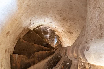 Fotobehang Gang Old stone spiral staircase in a castle or old Church. Bottom view of the stairs and narrow passage. Historical value and culture.  © Pokoman