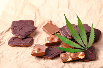 Organic Marijuana Pieces of Chocolate with CBD cannabis nuts and dry green hemp leaves. Chocolate coated hemp biscuits. Marijuana sweet food concept