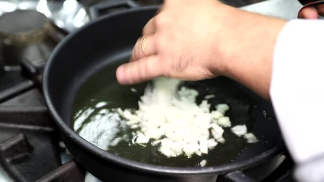 Cocinero a&ntilde;adiendo cebolla a una sart&eacute;n