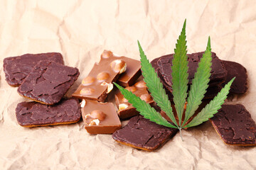 Pieces of delicious chocolate and cookies on the background of wrapping paper with a green hemp leaf. Cannabis Leaf Vegan Chocolate with CBD Supplement and Green Marijuana Leaves