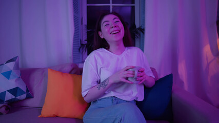 Happy asian woman drinking coffee and watching tv in evening at home