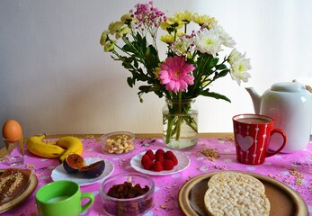 Obraz na płótnie Canvas Colorful breakfast table with flowers and healthy food such as fruit, chocolate, rice cakes or bread
