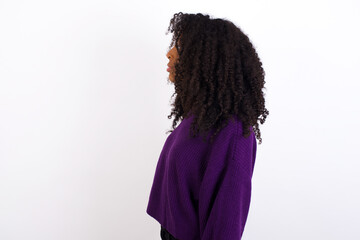 Young beautiful African American woman wearing knitted sweater against white wall,  looking to side, relax profile pose with natural face with confident smile.