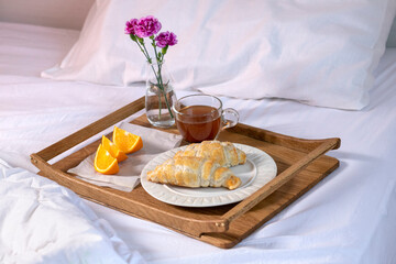 Wooden tray with a cup of tea and croissants and orange slices. Breakfast in bed. Good morning concept