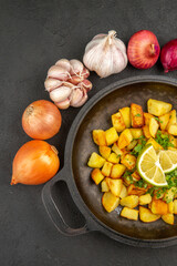 top view tasty fried potatoes inside pan with lemon and garlics around on a dark background color calorie cuisine meal food