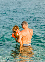 Grandfather carrying toddler girl with swimmies in sea