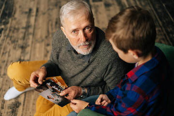 Top view of handsome bearded gray-haired grandfather with his grandson having fun looking at an old photo album, enjoying memories watching family photo album at home in living room