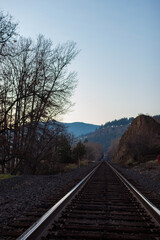 Fototapeta premium Landscape in late autumn at sunset, in the center of the railway, in front of the horizon blue mountains.