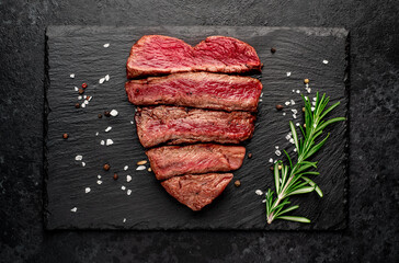 Different degrees of roasting beef steak in heart shape with spices on a stone background