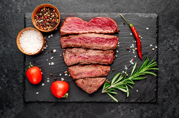 Different degrees of roasting beef steak in heart shape with spices on a stone background