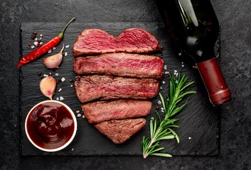 Poster Different degrees of roasting heart-shaped beef steak with spices and bottle of wine on a stone background. valentines day celebration concept © александр таланцев