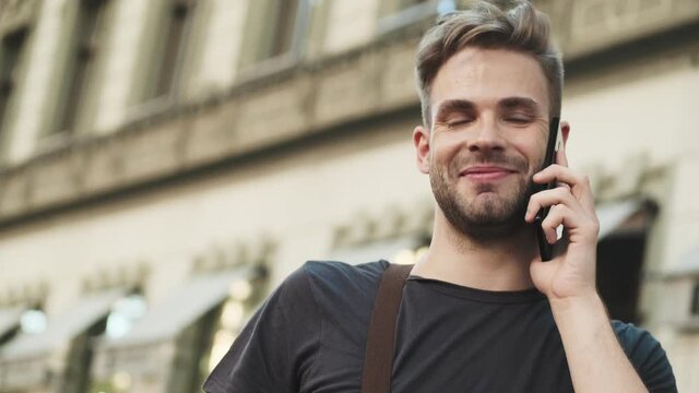Young cheerful positive man talking by mobile phone outdoors on the street