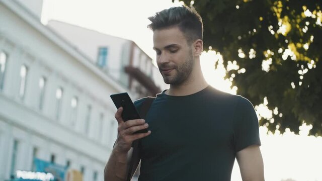 Young optimistic man using mobile phone outdoors on the street