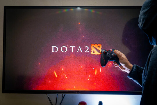 Man holding a steam controller and playing popular video game DOTA 2 on a television and PC
