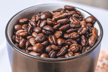 Black mug full with roasted coffee grains on a bamboo mat from a top view. Concept of pure caffeine