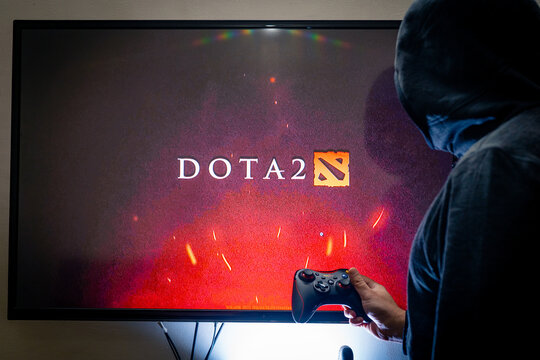 Man holding a steam controller and playing popular video game DOTA 2 on a television and PC
