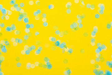 Blue green and yellow paper confetti on a vibrant yellow background