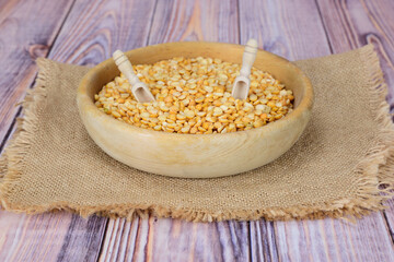 A wooden bowl of dry peas with two scoops stuck in on a coarse napkin.