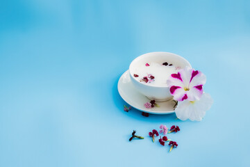 White Cup with vegan milk and flowers on a blue background. Concept of vegetarian drinks and food, herbal teas, beauty and health, Spa