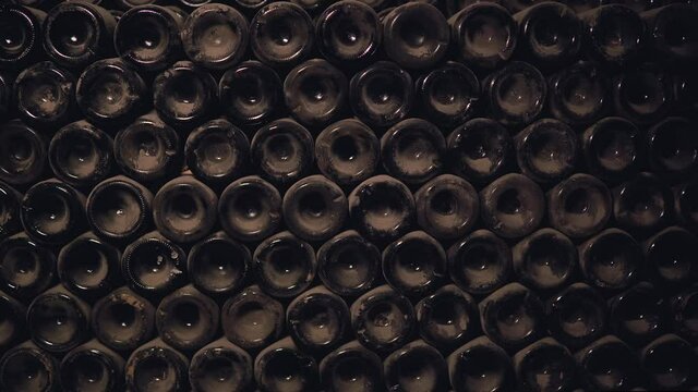 Close-up shot, old bottles of wine in a cellar. Glass wine cabinets covered with dust due to long storage. Warm, muted tones. Collection wine in the cellar, sealed in bottles and stacked under a stone