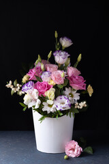 delicate bouquet of roses, daisies, chrysanthemums, unopened buds in a white round box, a sprig of lisianthus on a gray table and a black background.