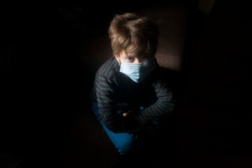 niño rubio con mascarilla quirúrgica mirando hacia arriba con luz tenue 