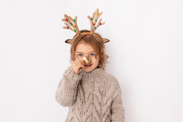 little girl with deer antlers and Christmas ball on her nose on white background, space for text, new year and Christmas concept