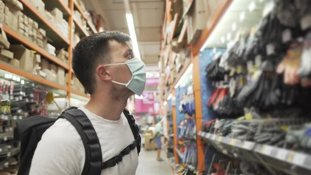 Client male Caucasian professional master chooses protective equipment in hardware hypermarket, wearing medical mask face, DIY. Social distancing restrictions during coronavirus epidemic shopping