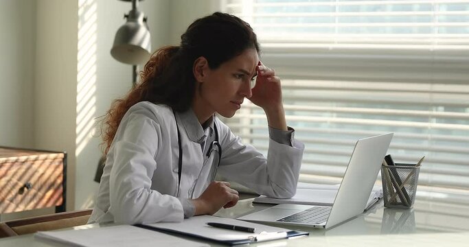Female doctor in white uniform sit at desk read news on laptop learn information statistics of coronavirus infected patients feels stressed, problems at work, professional failure, dismissal concept