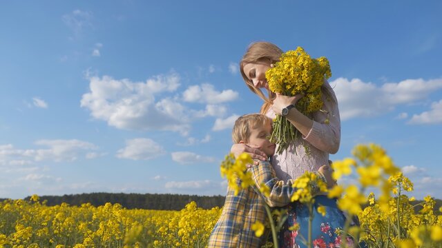 A loving son hugs his mother in a rapeseed field.