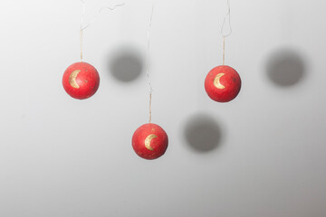 3 bolas rojas de decoración navideñas suspendidas en el aire con lunas doradas estampadas y sombra circular proyectada en la pared