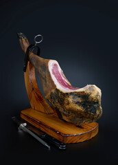 Spanish Iberian serrano ham in wooden support. Isolated on elegant dark background