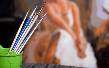 Paint brushes in a bucket. Drawing by numbers. Against the background of the painted picture. The picture is out of focus.