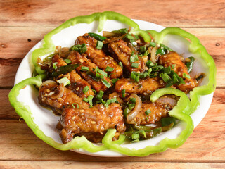 Paneer chilli is Indo Chinese cuisine dish, Paneer cubes tossed with tomatoes, onions, spring onions, chilli sauce. served over a rustic wooden background, selective focus
