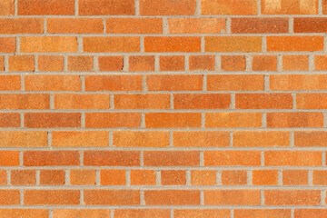 Full frame texture background of a grungy vintage brick wall in common bond pattern, with bricks in varying shades of orange and red, having a subtle shimmering surface patina.