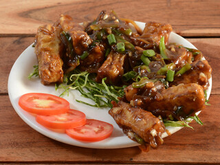 Paneer chilli is Indo Chinese cuisine dish, Paneer cubes tossed with tomatoes, onions, spring onions, chilli sauce. served over a rustic wooden background, selective focus